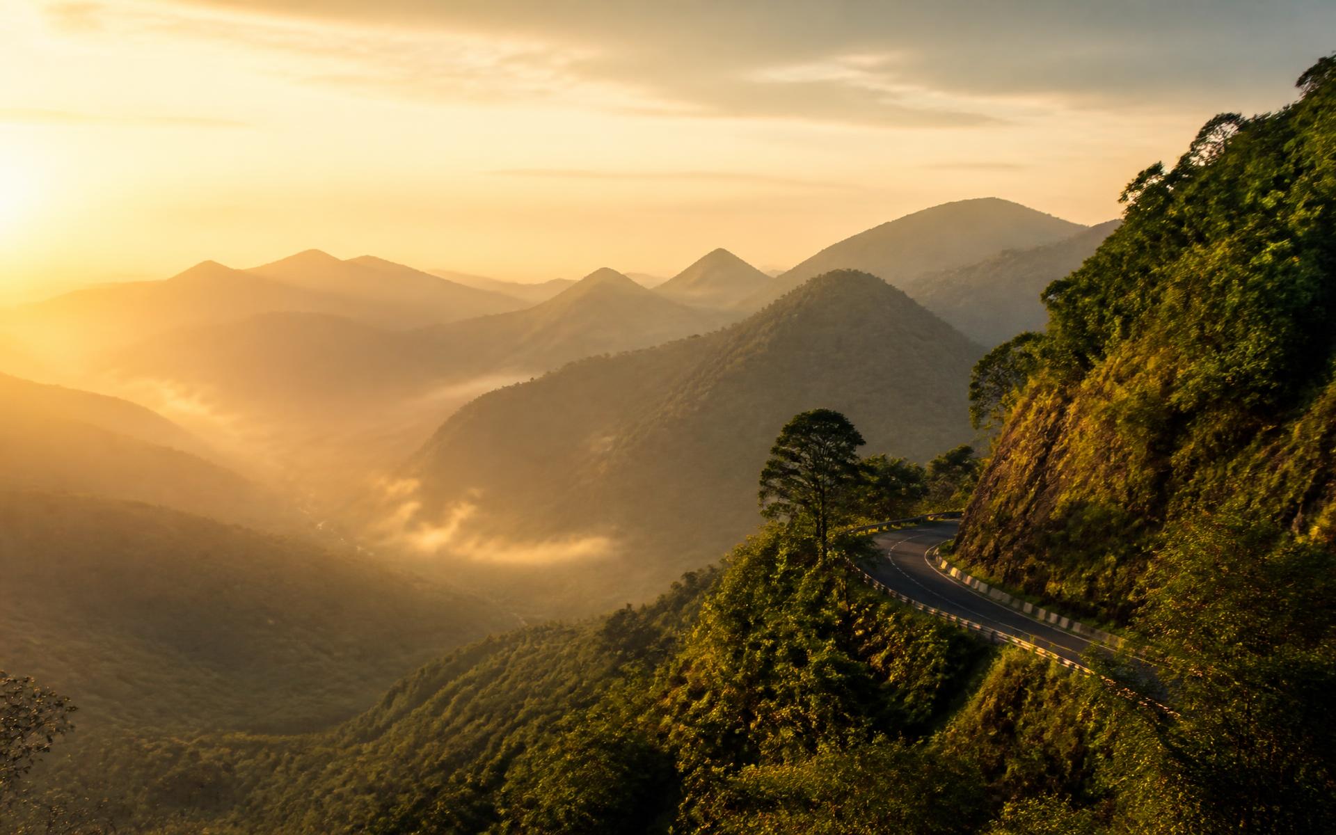 Misty layered mountains and a winding road in the Western Ghats at sunrise